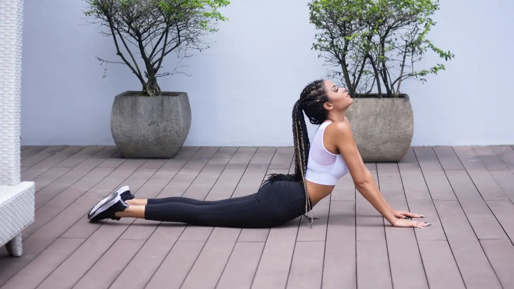 Cô gái tóc tết tập tư thế rắn hổ mang trên sàn gỗ ngoài trời
