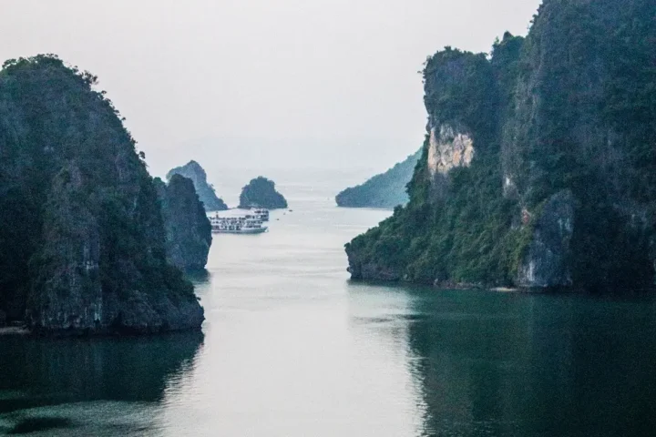 Lạch nước giữa các đảo đá vôi, tàu khách nhỏ phía xa