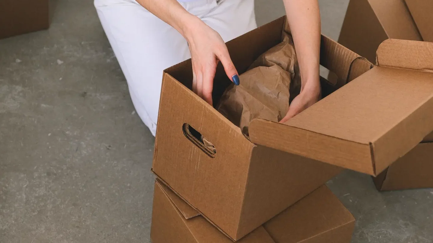 Tay người đang xếp đồ đã bọc giấy vào thùng carton