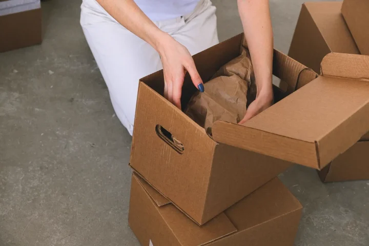 Tay người đang xếp đồ đã bọc giấy vào thùng carton