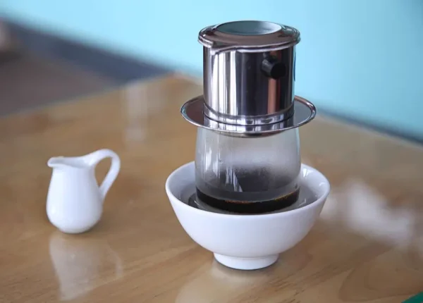 Phin nhôm đặt trên ly thuỷ tinh trong chén sứ trắng
