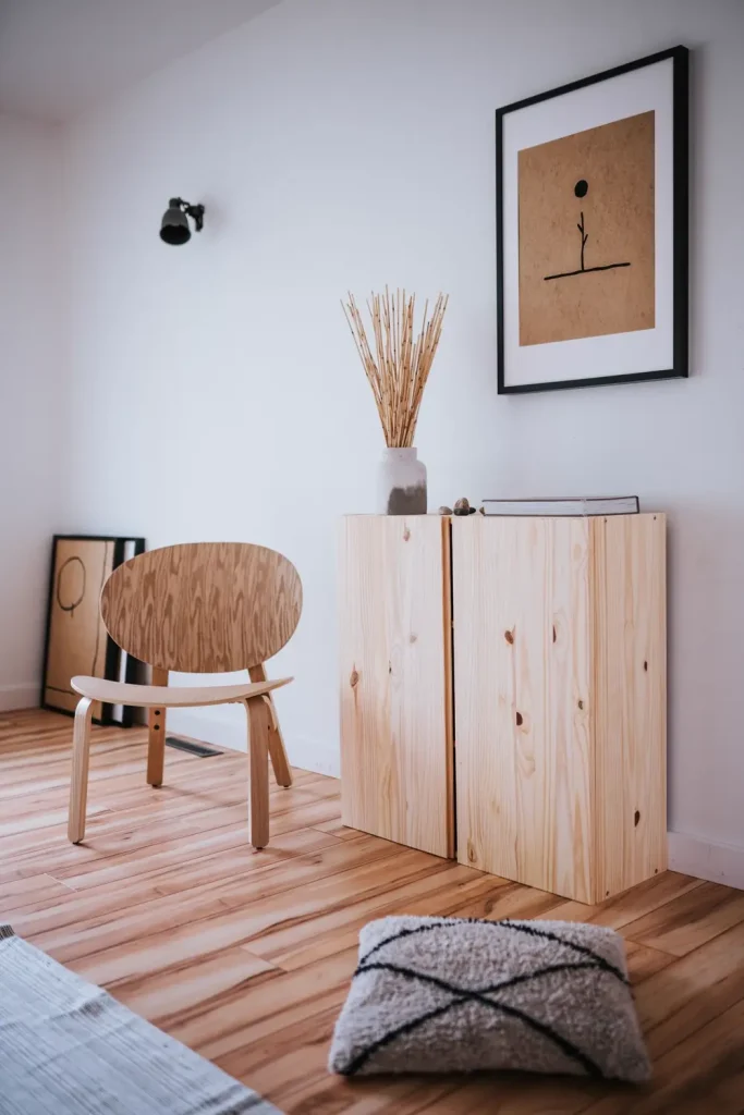 Ghế gỗ dán cong bên tủ gỗ thông, bình cỏ khô và tranh treo tường