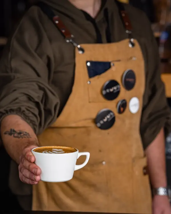 Thợ pha đeo tạp dề da đưa tách latte