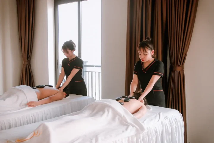 Hai chuyên viên massage đá nóng cho hai khách bên cửa sổ