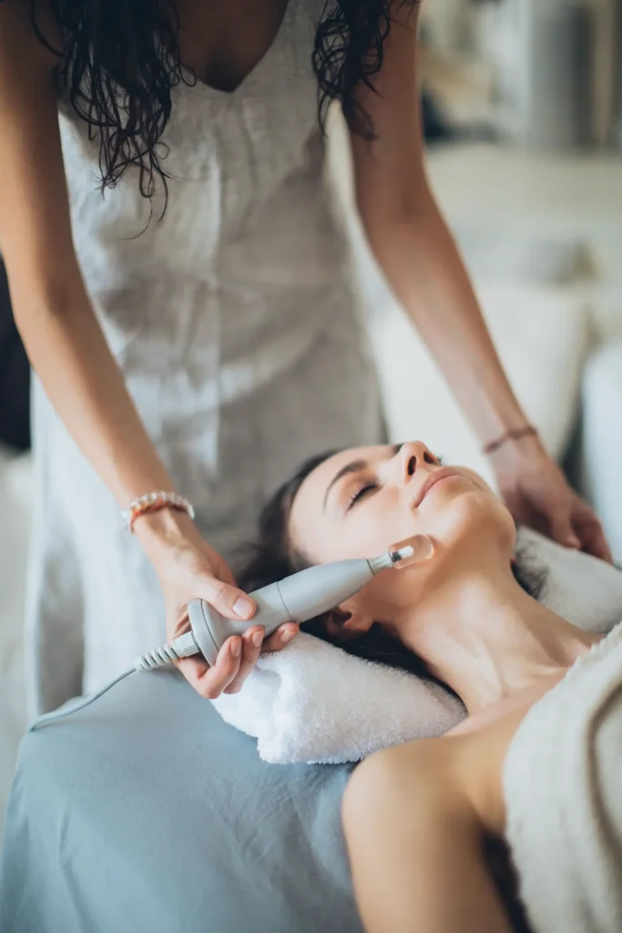Chuyên viên dùng máy chăm sóc da mặt cho khách đang nằm
