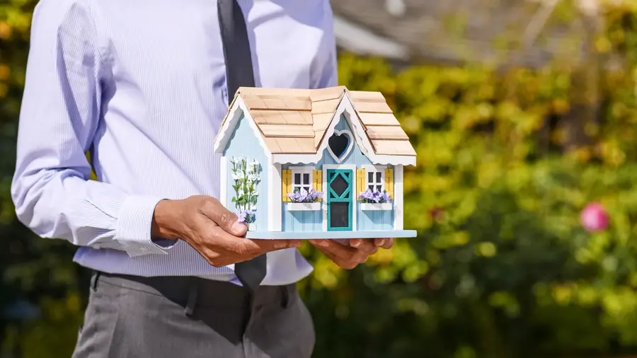 Đôi tay cầm mô hình ngôi nhà nhỏ, tượng trưng kế hoạch tài chính cho gia đình