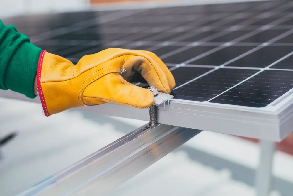 Bàn tay đeo găng bảo hộ siết kẹp khung tấm pin mặt trời