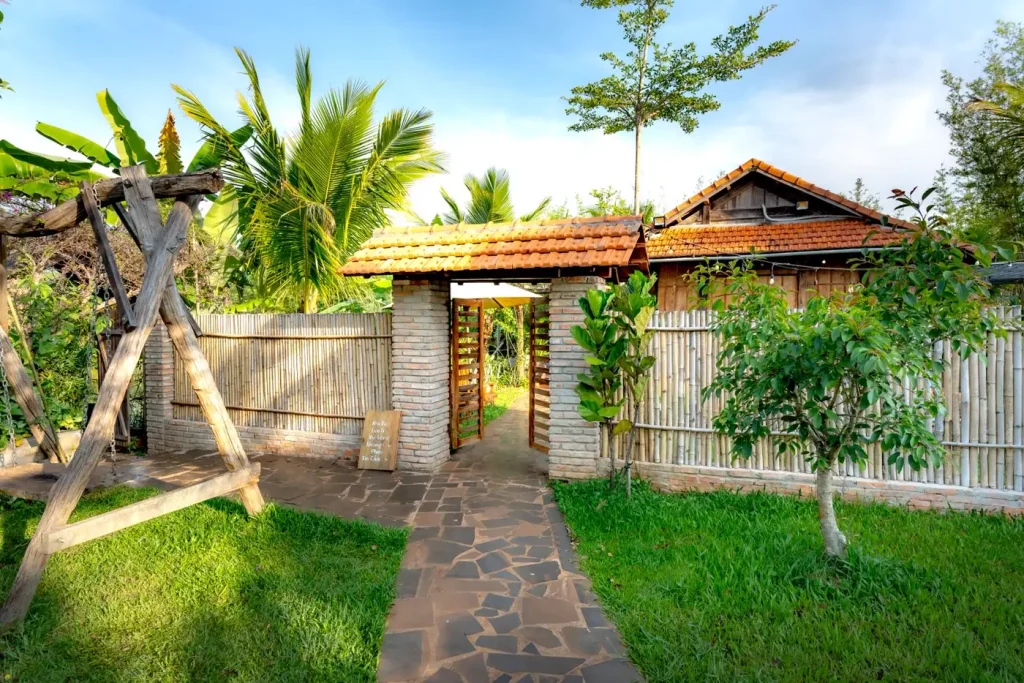 Cổng gạch mái ngói và lối đá dẫn vào vườn homestay