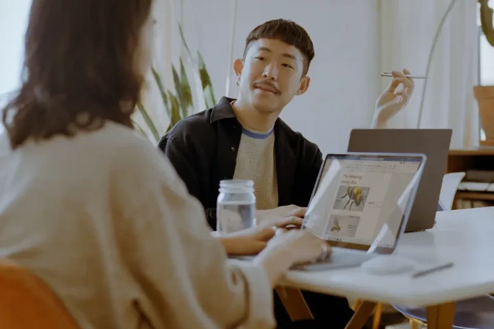 Hai đồng nghiệp trò chuyện bên máy tính xách tay trong văn phòng sáng