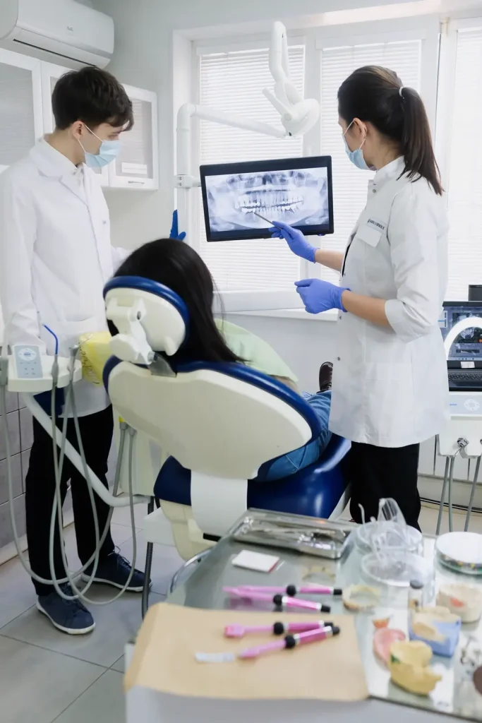 Hai bác sĩ xem phim X-quang răng cùng bệnh nhân trên ghế điều trị