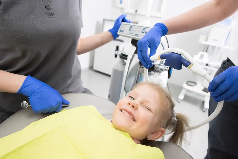 Bé gái nằm ghế nha khoa cười nheo mắt