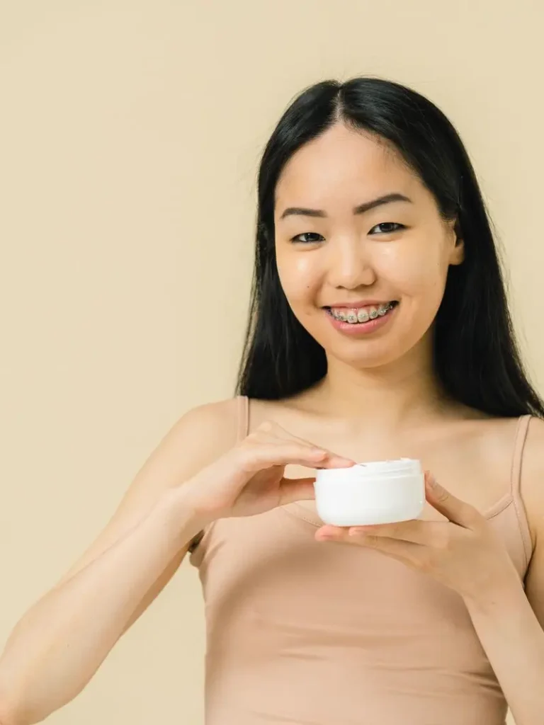 Cô gái mỉm cười cầm hũ kem dưỡng trên nền be