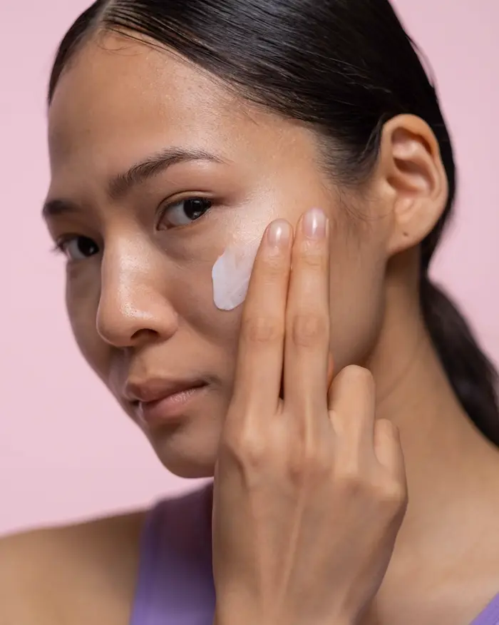 Cô gái chấm kem lên má, nền hồng