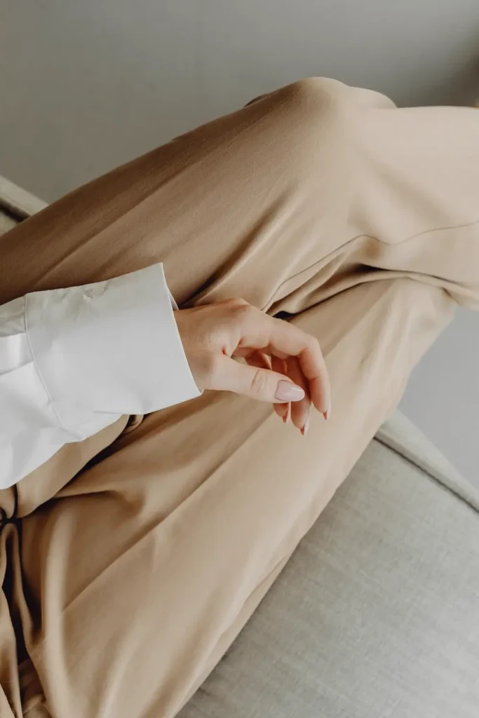 Bàn tay đặt trên quần vải màu be, tay áo sơ mi trắng